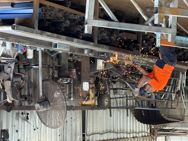 Grinder throwing sparks over a bench of angle and channel offcuts